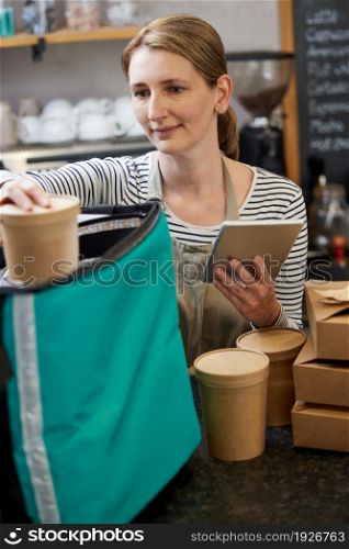 Female Restaurant Worker With Digital Tablet Packing Insulated Bag For Takeaway Food Home Delivery