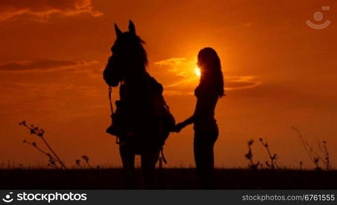 Female rider riding horse to horizon at sunset long shot