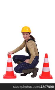 Female road worker kneeling by cones