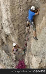 Female rock climber looking at a male rock climber scaling a rock face