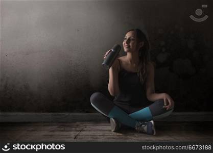 Female runner drinking water sitting legs crossed on floor