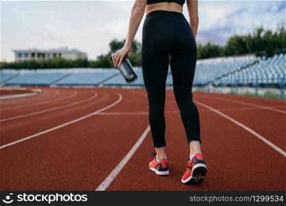Female runner in sportswear, back view, training on stadium. Woman doing stretching exercise before running on outdoor arena