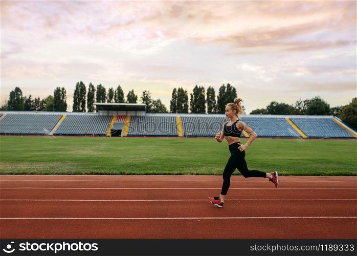 Female runner in sportswear jogging, training on stadium. Woman doing stretching exercise before running on outdoor arena