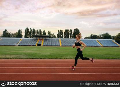 Female runner in sportswear jogging, training on stadium. Woman doing stretching exercise before running on outdoor arena
