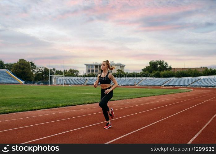 Female runner in sportswear jogging, training on stadium. Woman doing stretching exercise before running on outdoor arena. Female runner jogging, training on stadium