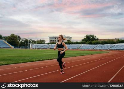 Female runner in sportswear jogging, training on stadium. Woman doing stretching exercise before running on outdoor arena. Female runner jogging, training on stadium