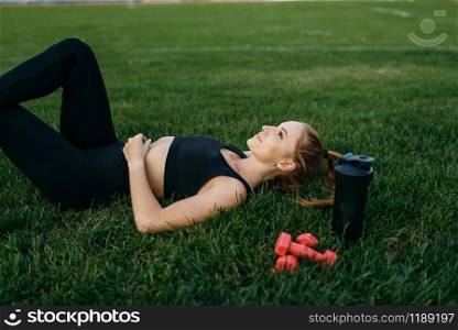 Female runner in sportswear lying on the grass, top view, workout on stadium. Woman doing stretching exercise before running on outdoor arena. Female runner lying on the grass, top view