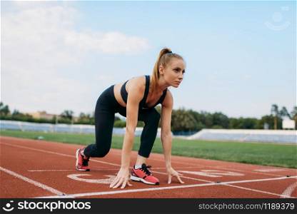 Female runner in sportswear on start line, training on stadium. Woman doing stretching exercise before running on outdoor arena