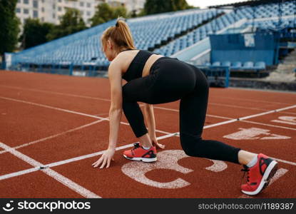 Female runner in sportswear on start line, training on stadium. Woman doing stretching exercise before running on sports arena. Female runner on start line, training on stadium