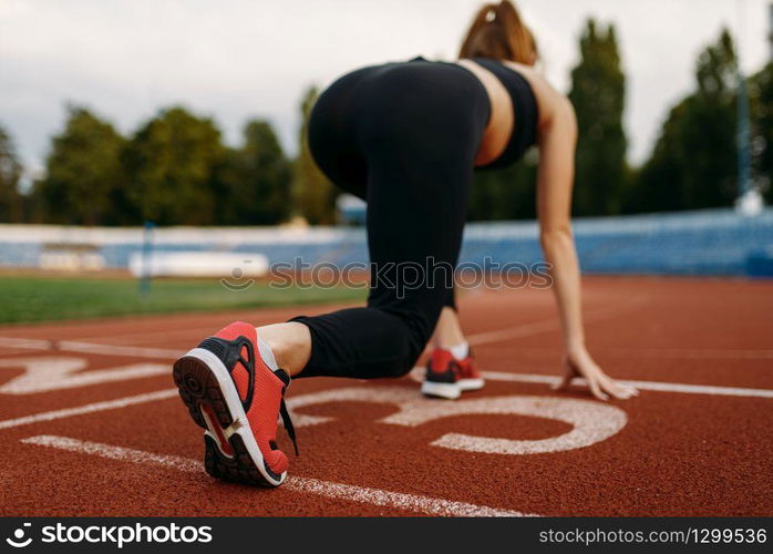 Female runner in sportswear on start line, training on stadium. Woman doing stretching exercise before running on outdoor arena. Female runner on start line, training on stadium