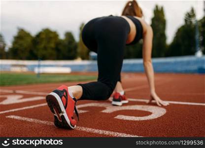 Female runner in sportswear on start line, training on stadium. Woman doing stretching exercise before running on outdoor arena. Female runner on start line, training on stadium