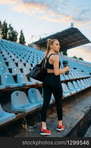 Female runner in sportswear on tribune, training on stadium. Woman doing stretching exercise before running on outdoor arena. Female runner in sportswear on stadium tribune