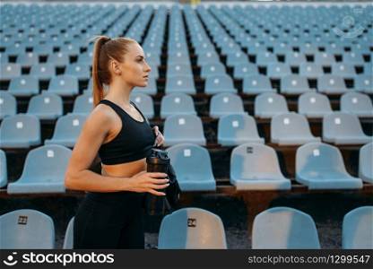 Female runner in sportswear on tribune, training on stadium. Woman doing stretching exercise before running on outdoor arena. Female runner in sportswear on stadium tribune