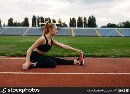 Female runner in sportswear, training on stadium. Woman doing stretching exercise before running on outdoor arena. Female runner in sportswear, training on stadium