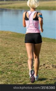 Female runner jogging by water park sunny day fit body
