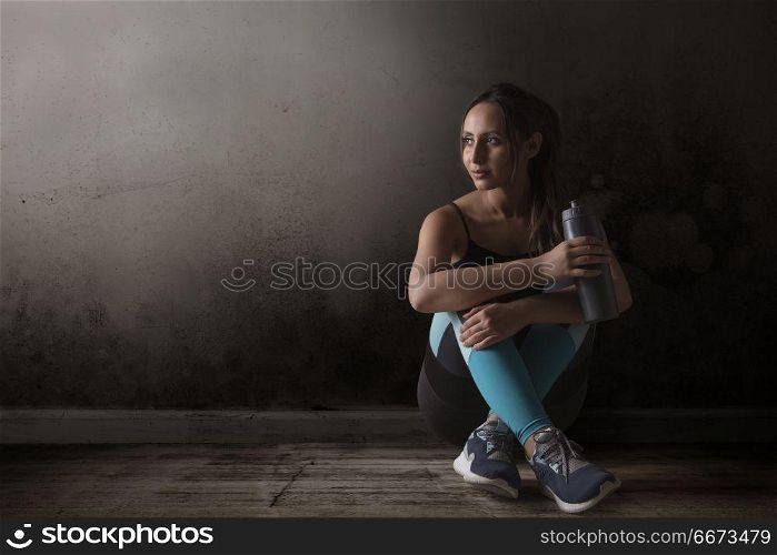 Female runner sitting legs crossed on floor holding water bottle