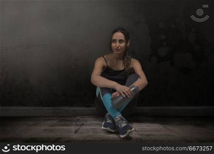 Female runner sitting legs crossed with water bottle on floor