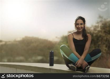 Female runner sitting legs crossed with water bottle on wall