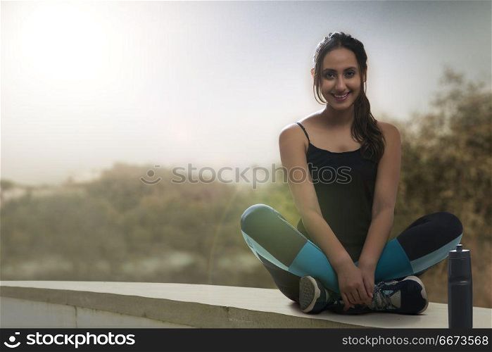 Female runner sitting legs crossed with water bottle on wall