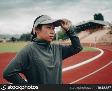 Female runners in a hat prepares for running on stadium track. Athletic woman in sport clothes jogging outdoors. Healthy lifestyle concept.