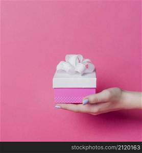 female s hand holding box with white ribbon bow pink background