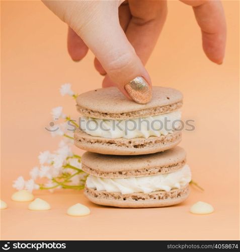 female s hand with golden nail polish taking macaroon against colored backdrop