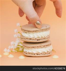 female s hand with golden nail polish taking macaroon against colored backdrop
