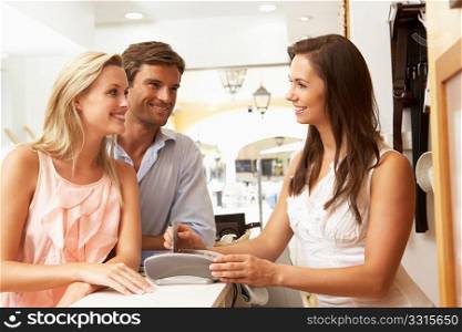 Female Sales Assistant At Checkout Of Clothing Store With Customers
