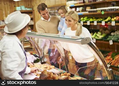 Female Sales Assistant Serving Family In Delicatessen