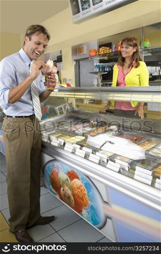 Female sales clerk looking at a mid adult man holding ice cream