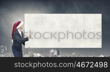 Female Santa with billboard. Woman in Santa hat pointing with finger at blank banner. Place for your text