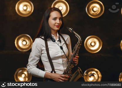 Female saxophonist plays the saxophone on the stage with spotlights. Jazz performer playing on the scene. Female saxophonist plays the saxophone on stage