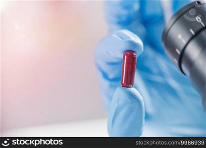 Female scientist holding red pill with blue gloves in laboratory. New Pill Research Concept. Scientist’s Hand in a Glove Holding an Red Pill