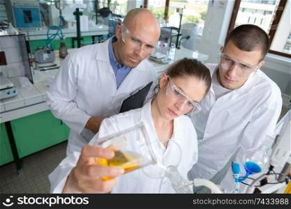 female scientist pouring liquid as teacher and classmate observe