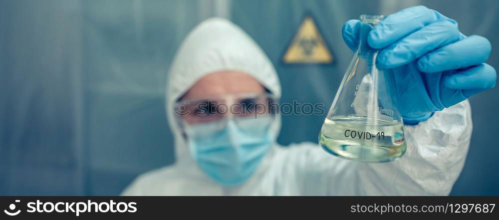Female scientist with bacteriological protection suit looking test tube in the laboratory. Selective focus on test tube in foreground