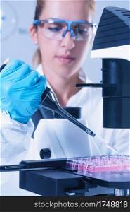 Female scientist with microscope, holding micro pipette