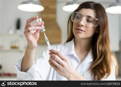 female scientist with safety glasses holding syringe with vaccine lab