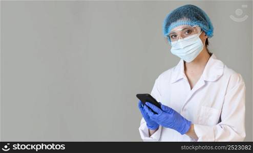 female scientist with safety glasses medical mask holding smartphone