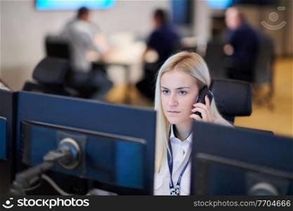 Female security guard operator talking on the phone while working at workstation with multiple displays Security guards working on multiple monitors