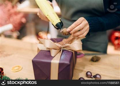 Female seller decorates gift box with fir cone, handmade wrapping and decoration process. Woman wraps present on the table, decor procedure