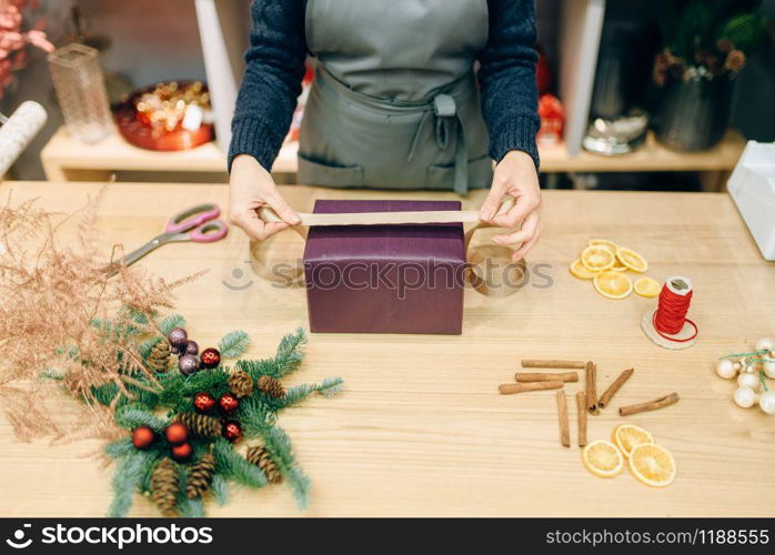 Female seller decorates gift box with wrapping paper and golden ribbon, decoration process. Woman wraps present on the table, decor procedure