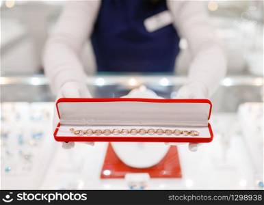 Female seller hands with gold bracelet in the case, jewelry store. Salewoman holds decorative box with golden decoration, jewellery shop