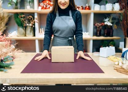 Female seller holds unwrapped carton gift box. Present wrapping papaer on the table, decoration procedure. Female seller holds unwrapped carton gift box