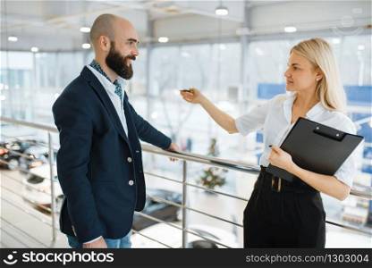 Female seller invites man to presentation in car dealership. Customer and saleswoman in vehicle showroom, male person buying transport, automobile dealer business. Seller invites man to presentation, car dealership