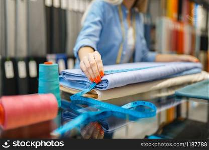 Female seller measures fabric in textile store. Shelf with cloth for sewing on background, clothing patterns choice in shop. Female seller measures fabric in textile store
