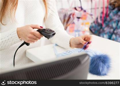 Female seller scanning winter hat at store. Seller holding barcode scanner in a hand