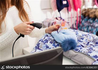 Female seller scanning winter hat at store. Seller holding barcode scanner in a hand