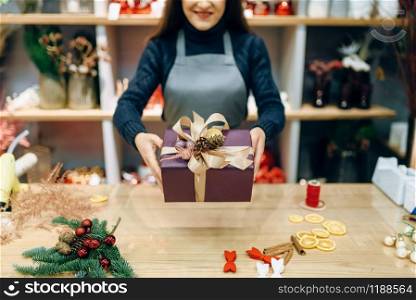 Female seller shows christmas gift box with handmade wrapping. Woman wraps present on the table, festive decor. Seller shows gift box with handmade wrapping