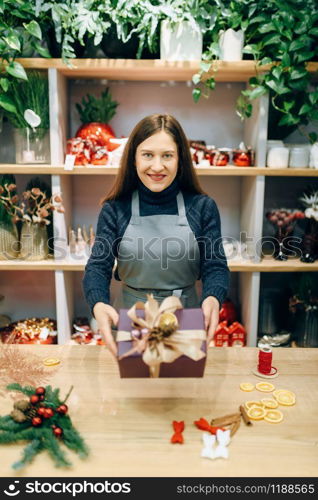 Female seller shows christmas gift box with handmade wrapping. Woman wraps present on the table, festive decor
