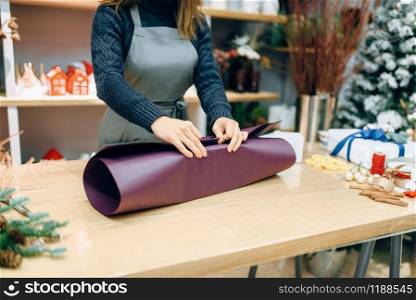Female seller wraps carton gift box in festive paper. Present wrapping on the table, decoration procedure